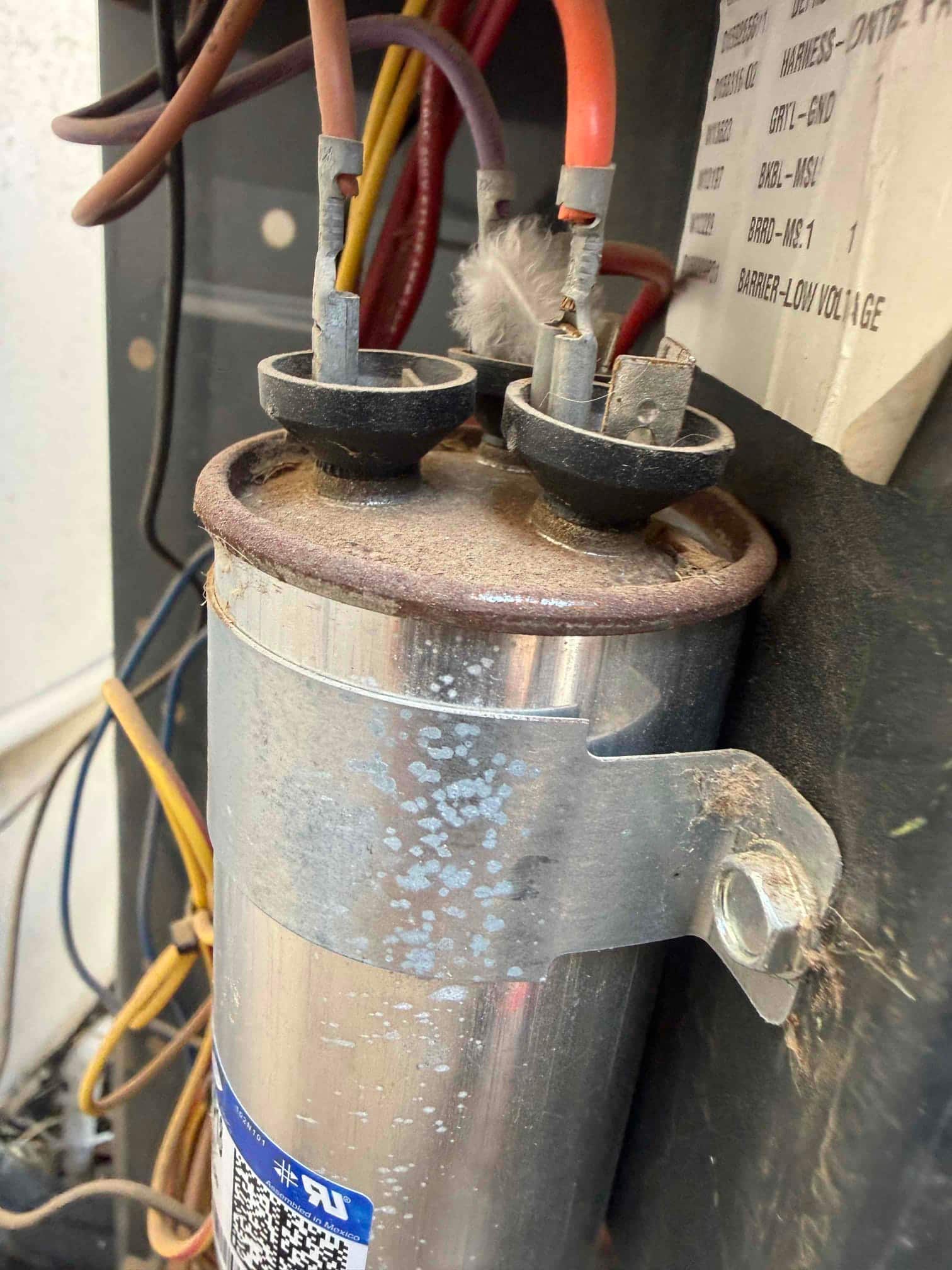 Failed run capacitor removed, showing swollen top and burnt terminal from thermal overload.