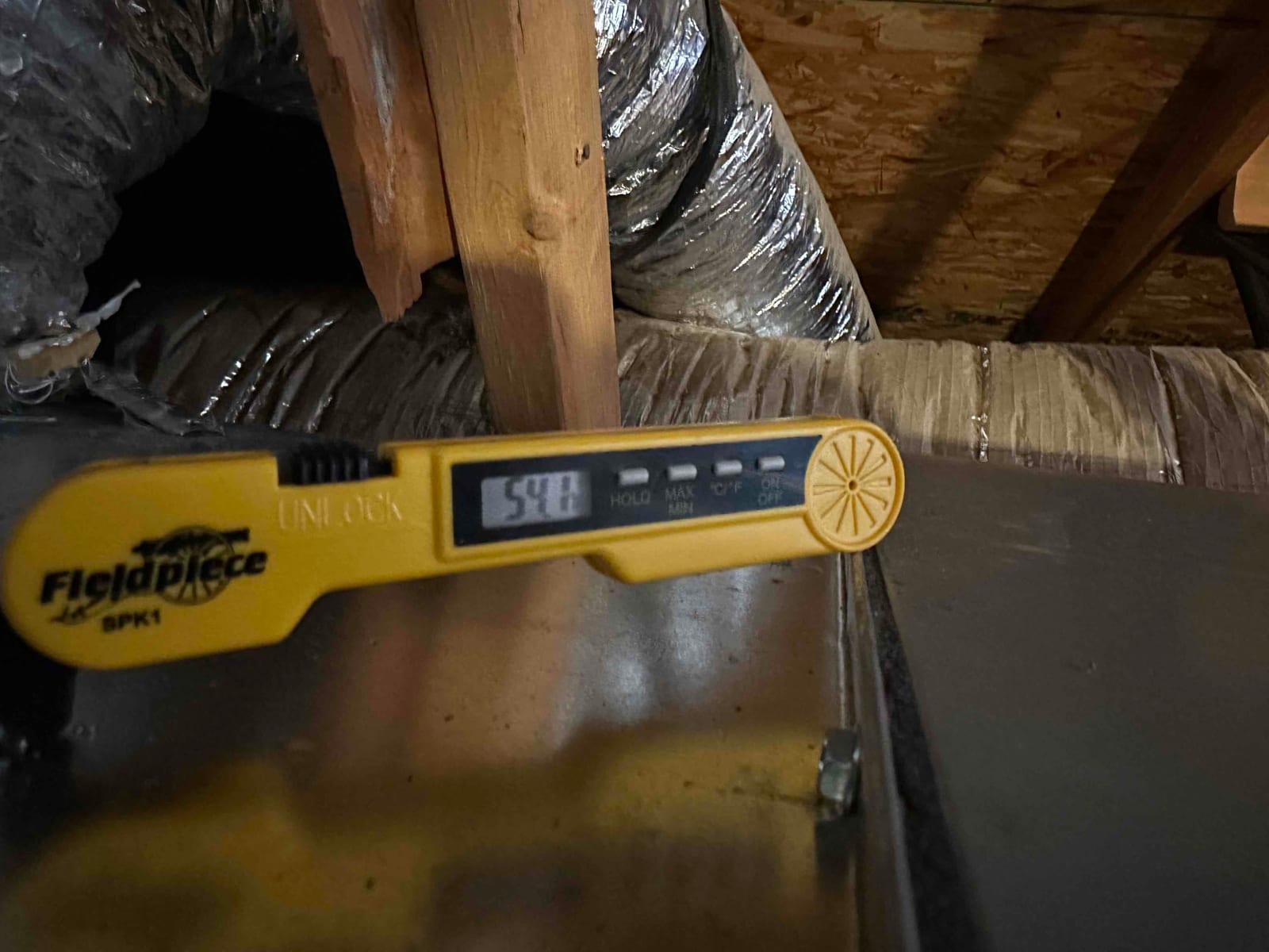Digital thermometer inserted at the supply plenum reads 54°F, documenting cooled supply air temperature during commissioning.