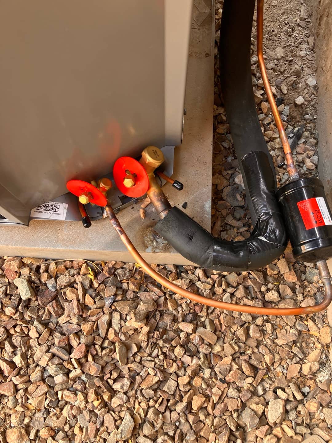 Final connections at the outdoor condenser showing insulated suction line, liquid line with filter-drier, and service valves with caps installed.