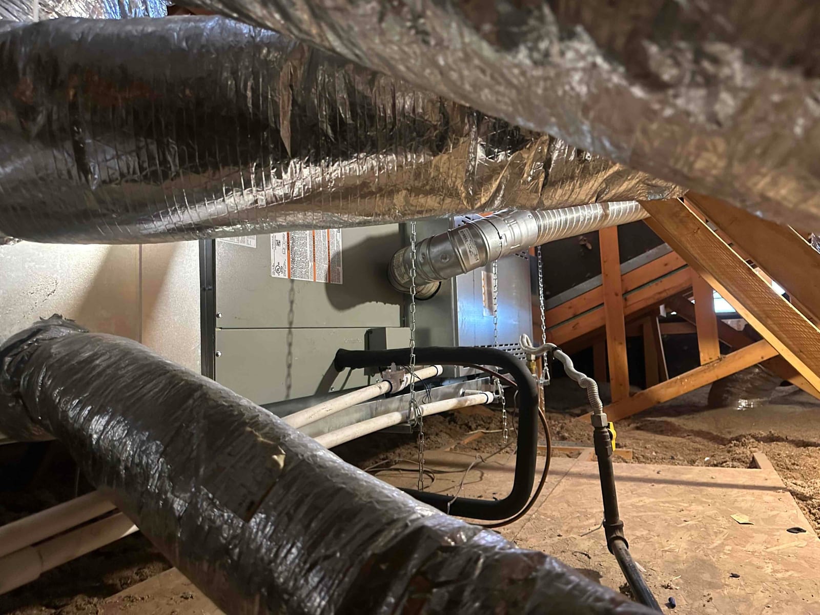 Horizontal attic air handler hung from chains with insulated flex ducts, condensate drain lines, and gas line routed nearby.