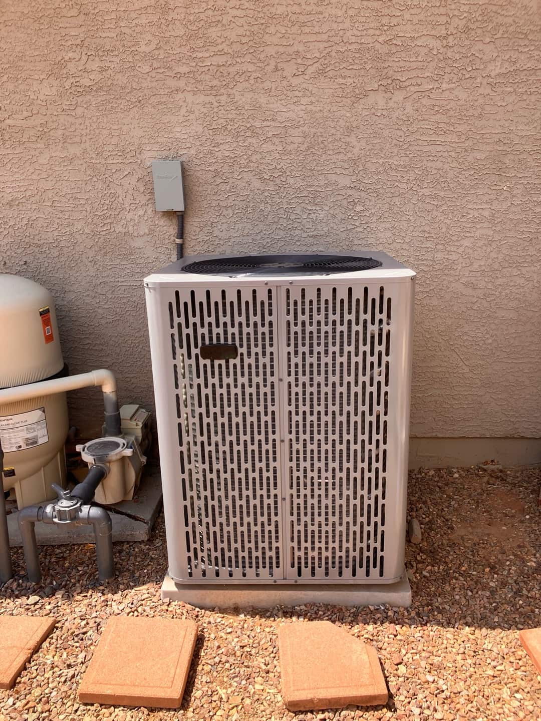 New outdoor condenser set on a level pad with nearby electrical disconnect and insulated line set penetration sealed at the wall.