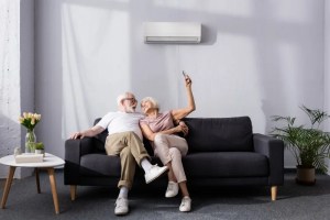 Happy senior couple relaxing on a couch under a wall-mounted unit after central AC installation.