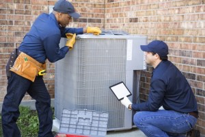 Two HVAC technicians performing AC installation service next to a brick wall.