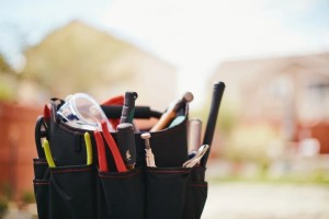 AC repair tool belt with pliers, safety goggles, and hand tools outdoors.