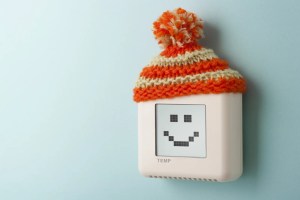 Wall thermostat with a smiley face display wearing a knit hat, symbolizing heating system installation.