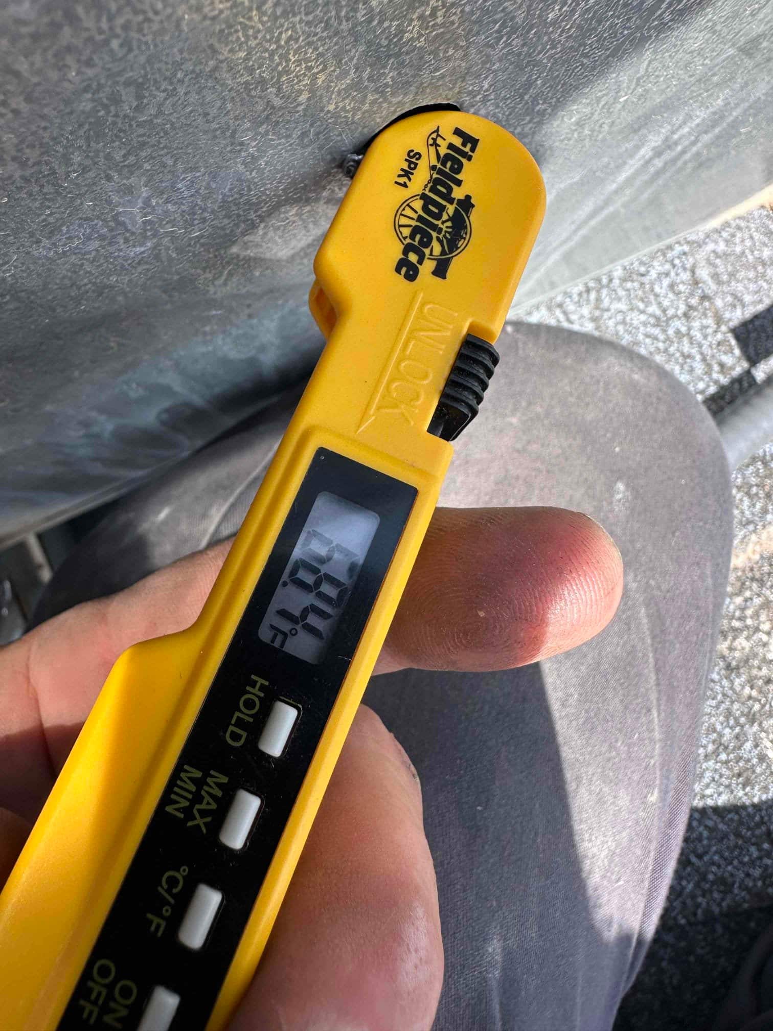 Digital thermometer probe shows 69.7°F while checking air temperature during HVAC system commissioning.