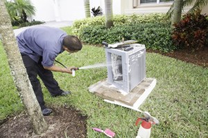 Technician performing AC maintenance service by cleaning an air conditioning unit on a lawn.