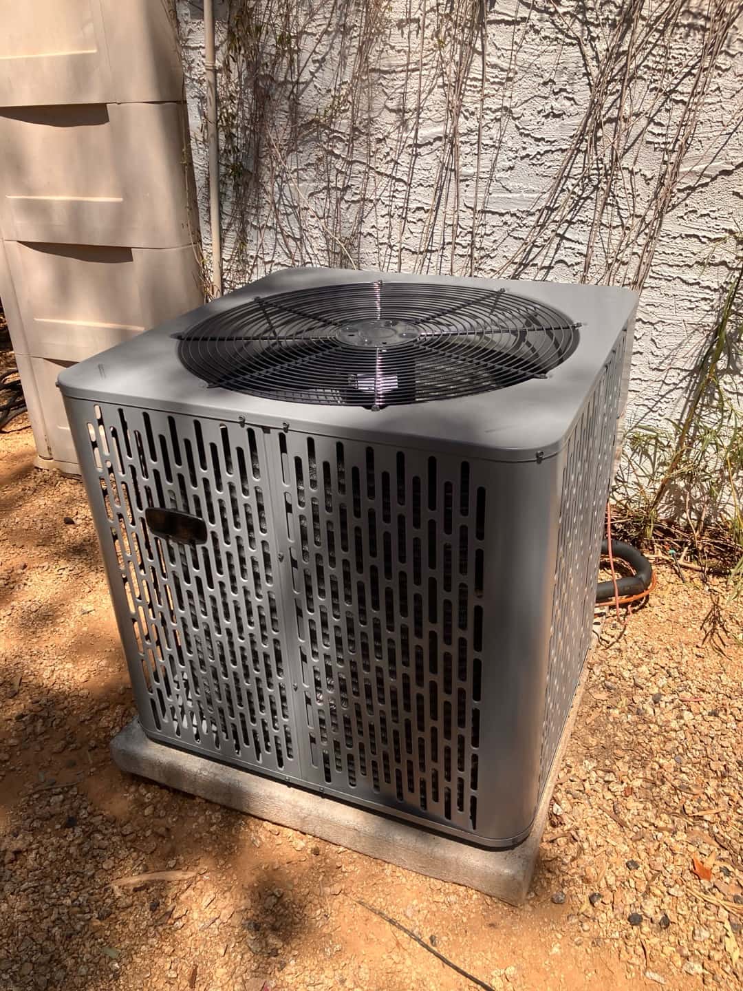 New outdoor heat pump condenser set on a level pad with insulated line set routed to the wall penetration.