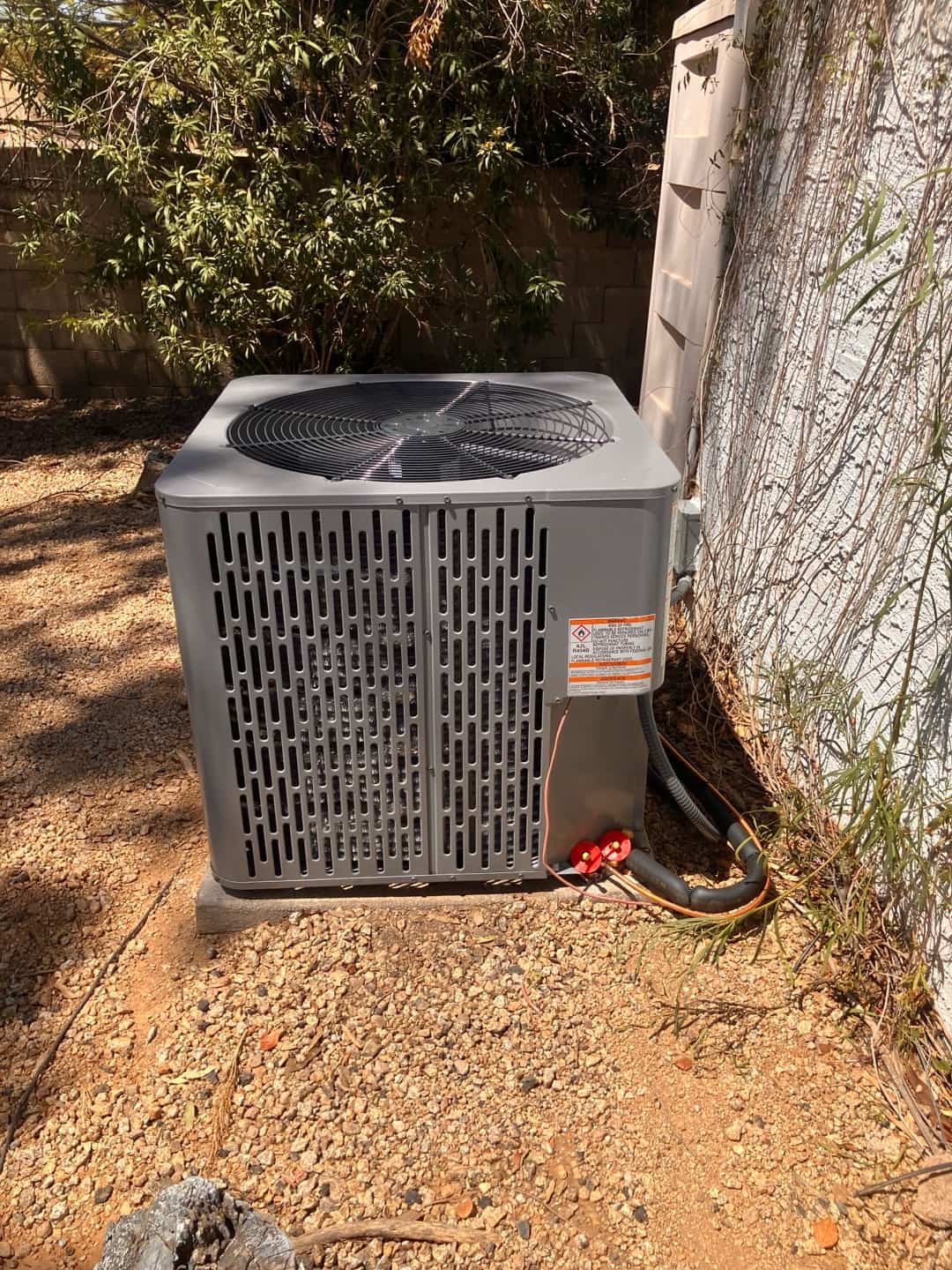 New outdoor heat pump condenser set on a level pad with insulated line set and sealed wall penetration.