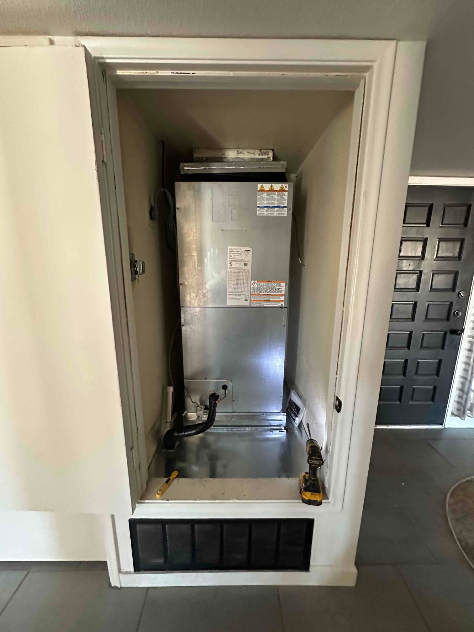 New vertical air handler set in a closet with condensate drain, return grille below, and tools staged for final connections.
