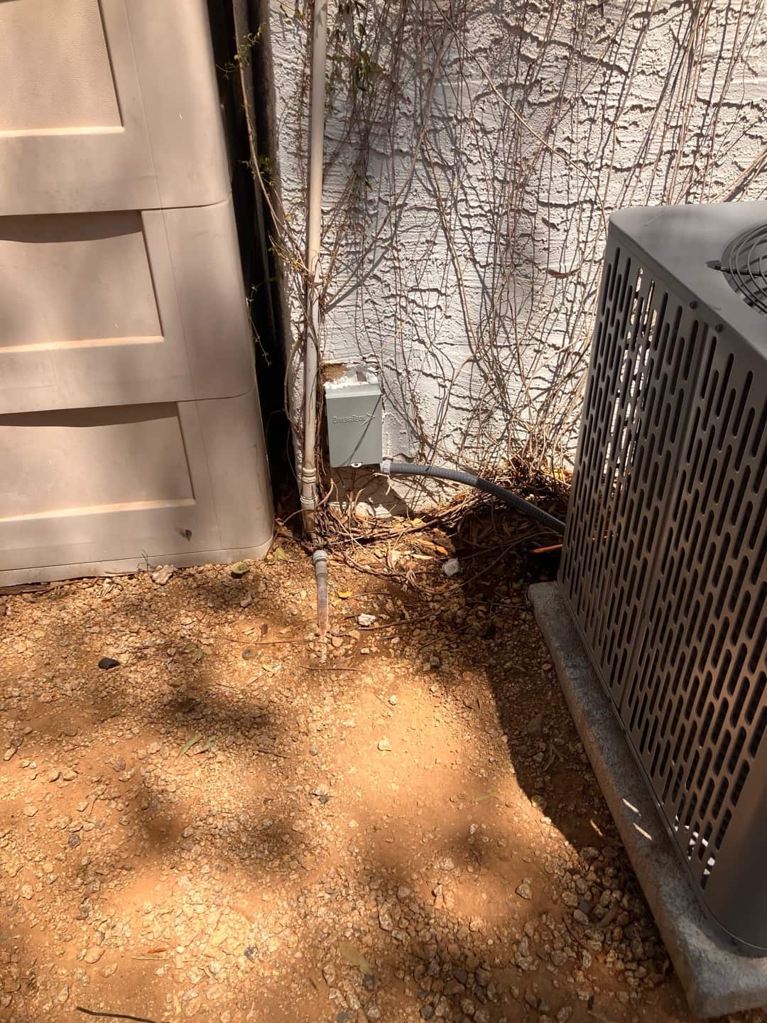 Outdoor heat pump condenser set on a pad with installed disconnect, line set, and insulated condensate drain termination.