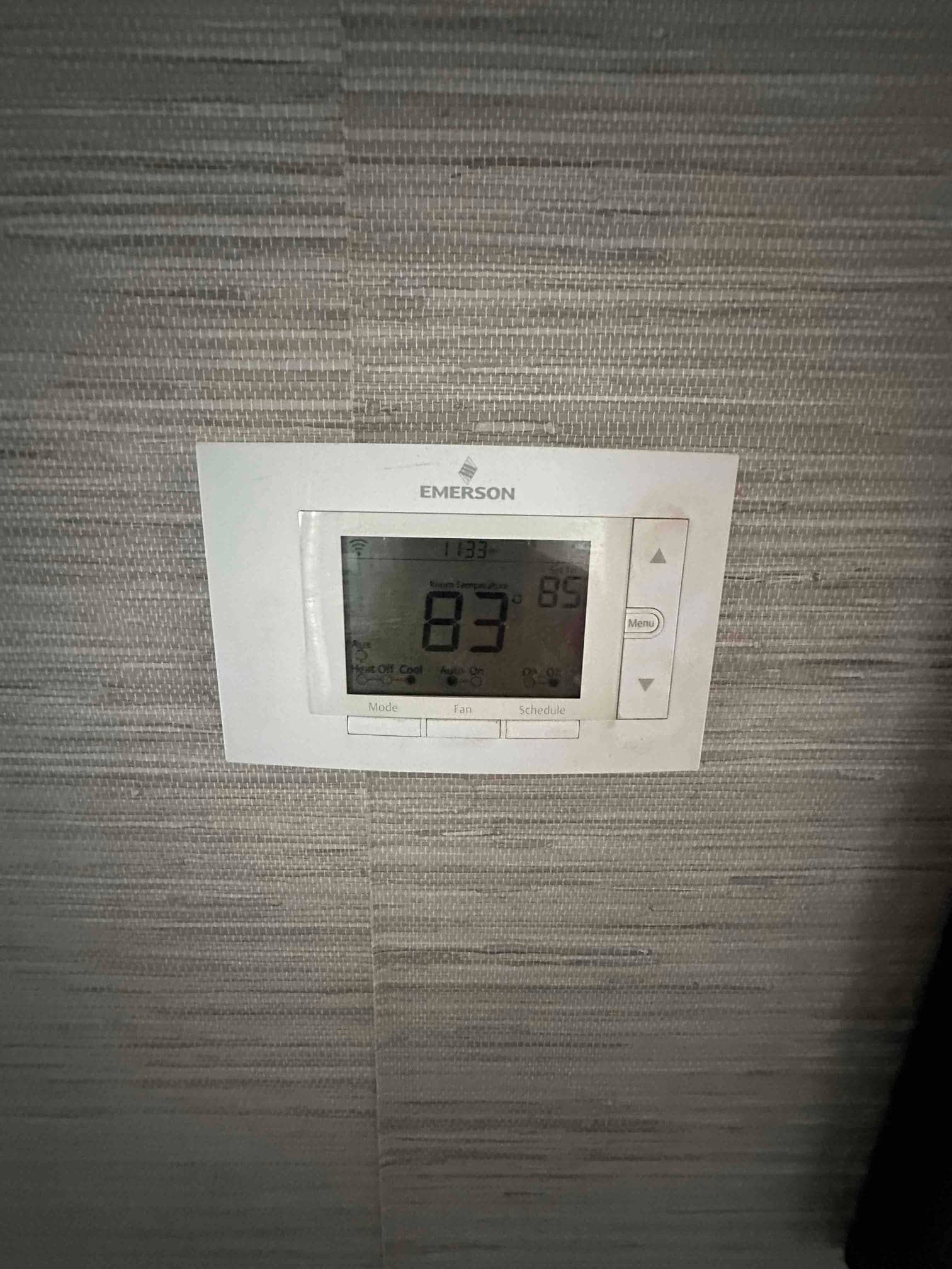 Wall-mounted digital thermostat installed and powered, displaying a room temperature of 83 degrees with control buttons visible.