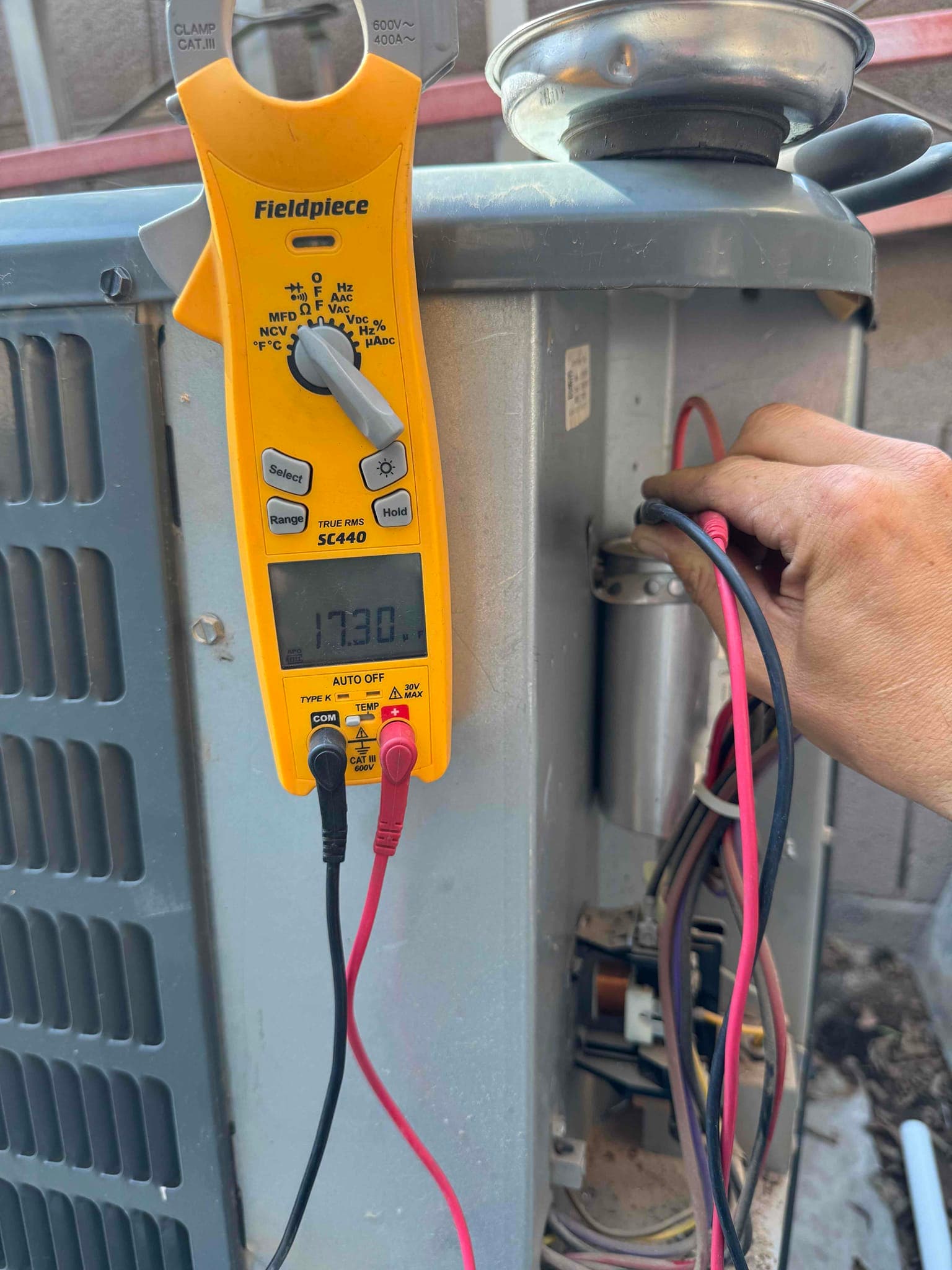Clamp meter displays 17.30 A while measuring current on a conductor at the outdoor condenser unit.