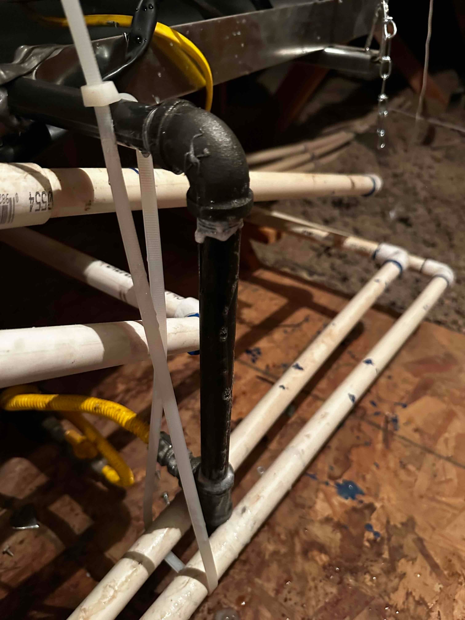 Condensate drain assembly in an attic, with PVC piping and a black vent tee secured by zip ties near the air handler.