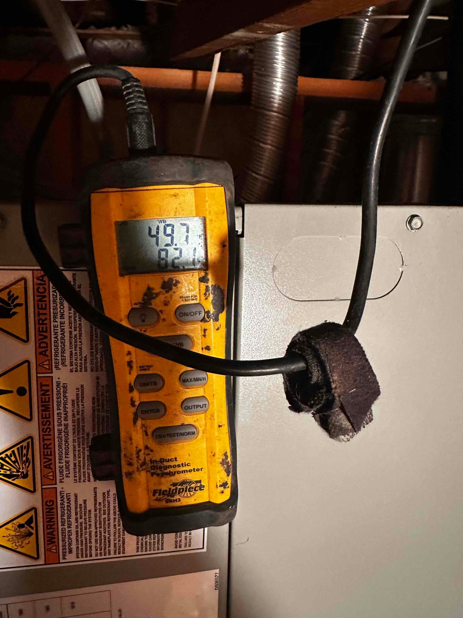 Digital in-duct thermometer displays 49.7°F with probe inserted at the air handler during supply air temperature check.