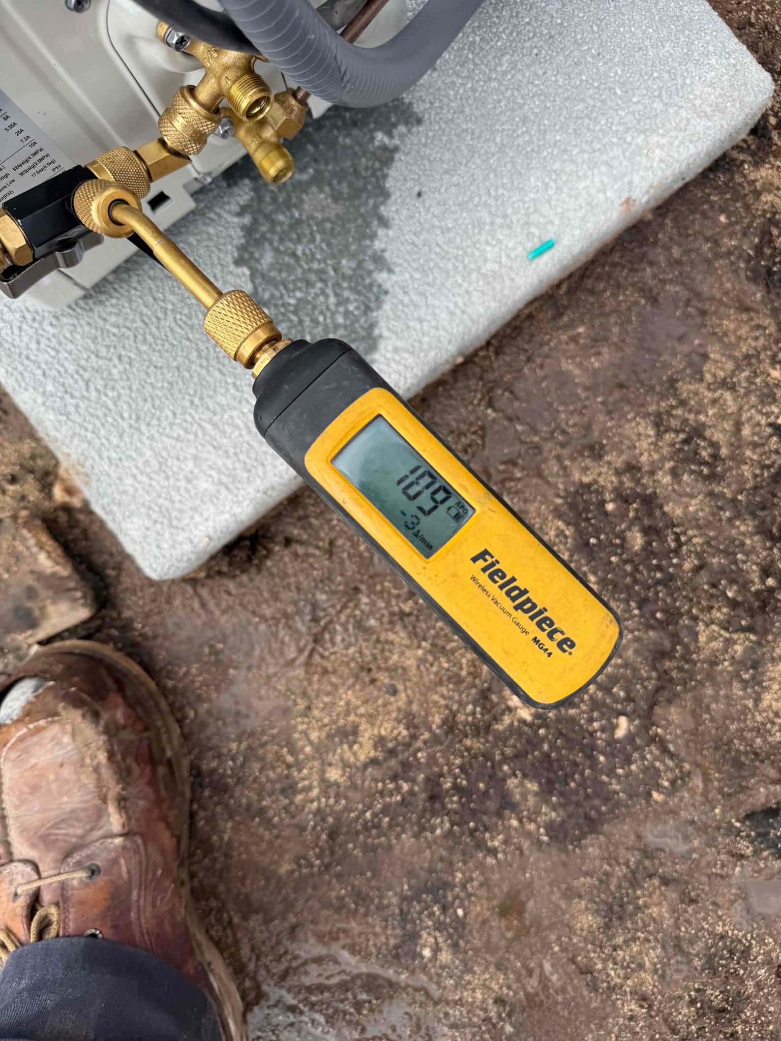 Digital micron gauge connected at the outdoor unit shows 189 microns, confirming a deep evacuation before releasing refrigerant.