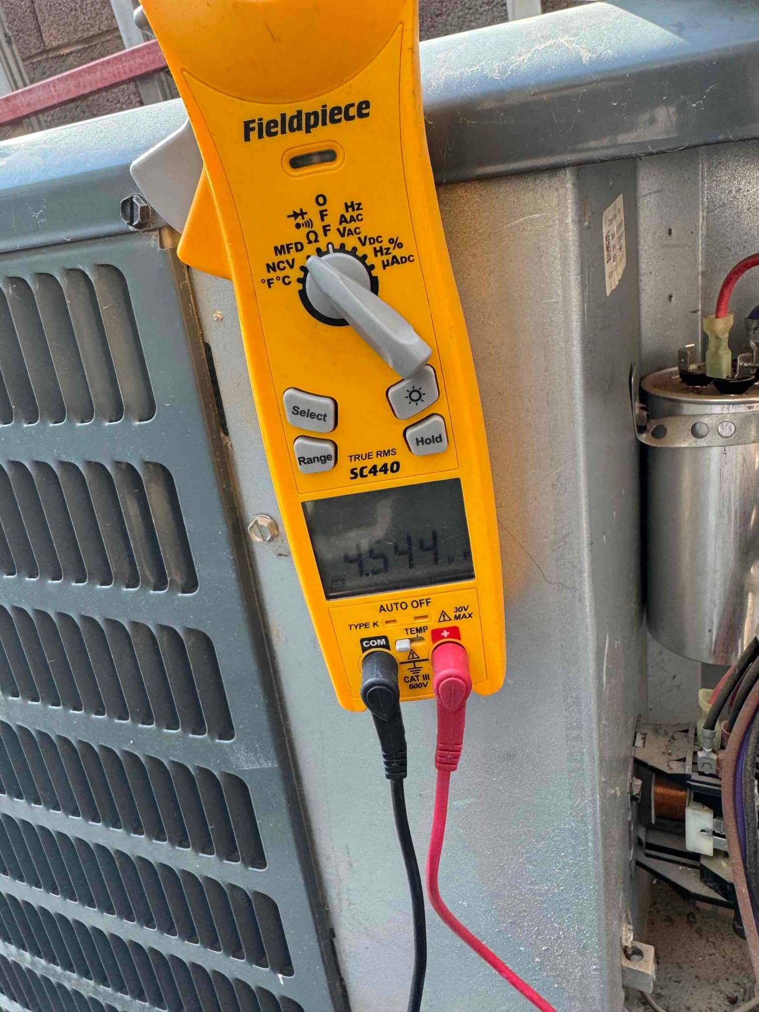 Digital multimeter measures capacitor at 45.44 μF beside the outdoor condenser unit during turbo run capacitor replacement.