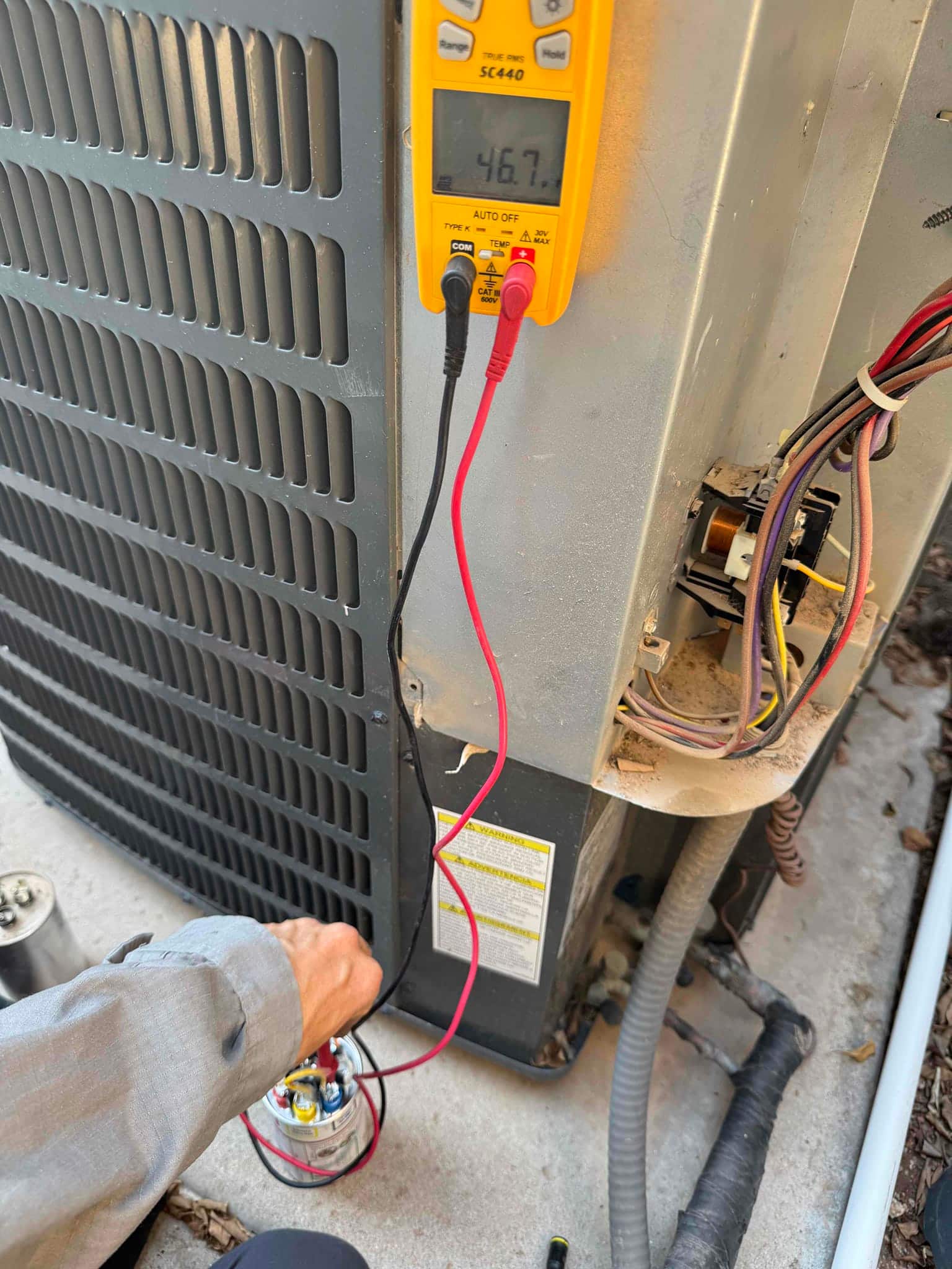 Digital multimeter measures the run capacitor at 46.7 μF while connected to the outdoor condenser’s capacitor terminals.