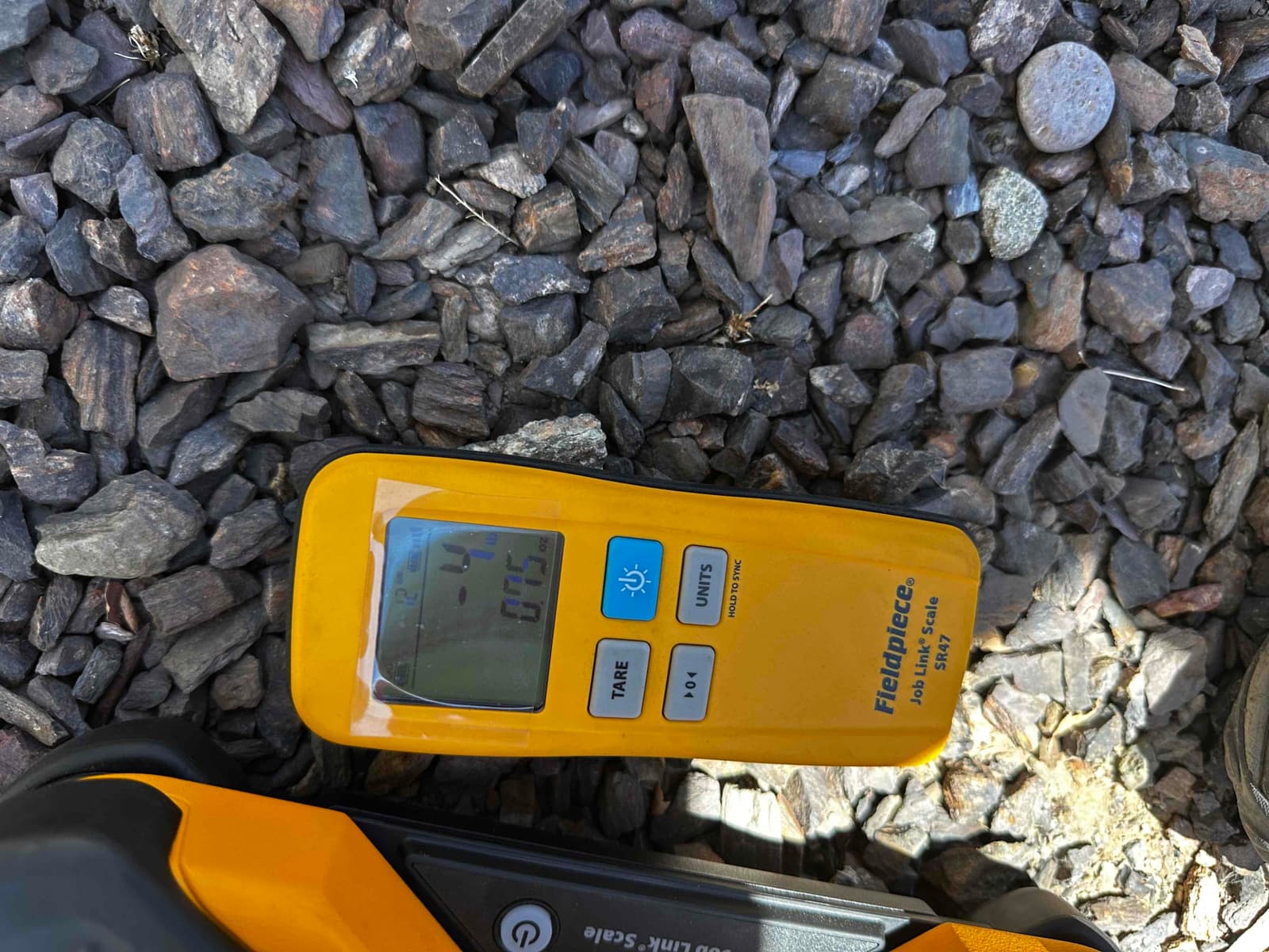 Digital refrigerant scale controller on gravel showing an illuminated display during HVAC installation work.