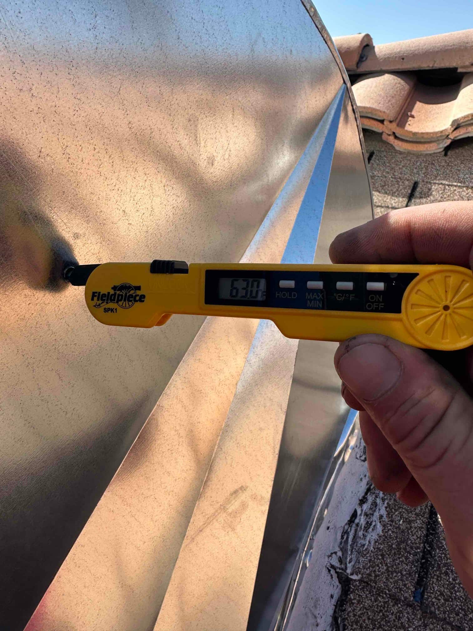 Digital thermometer shows 63.0°F while checking air temperature at a metal duct during commissioning.