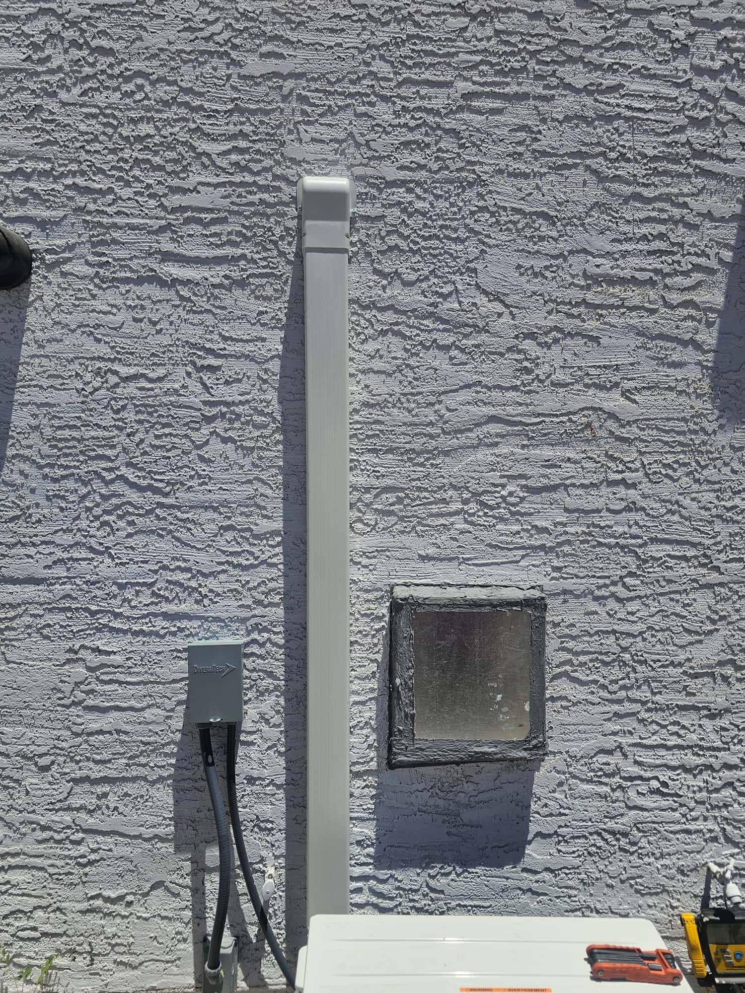 Exterior installation showing line-set cover, electrical disconnect with flexible conduit, and sealed wall penetration beside the new outdoor unit.
