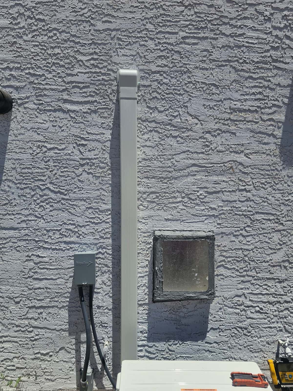Line-set cover installed vertically on exterior wall with new disconnect and sealed wall penetration beside mini-split outdoor unit.