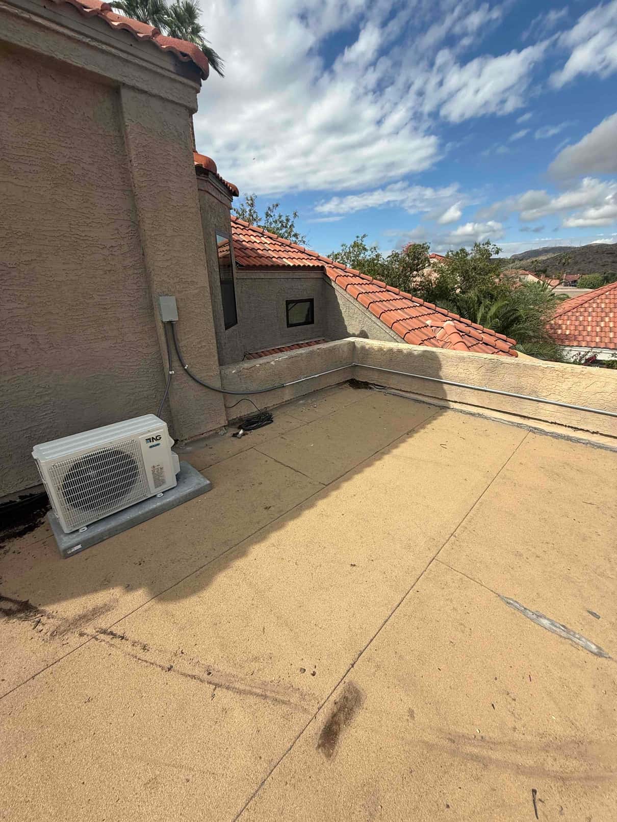 Mini-split outdoor condenser set on a rooftop pad with electrical whip and line set routed to the wall disconnect.