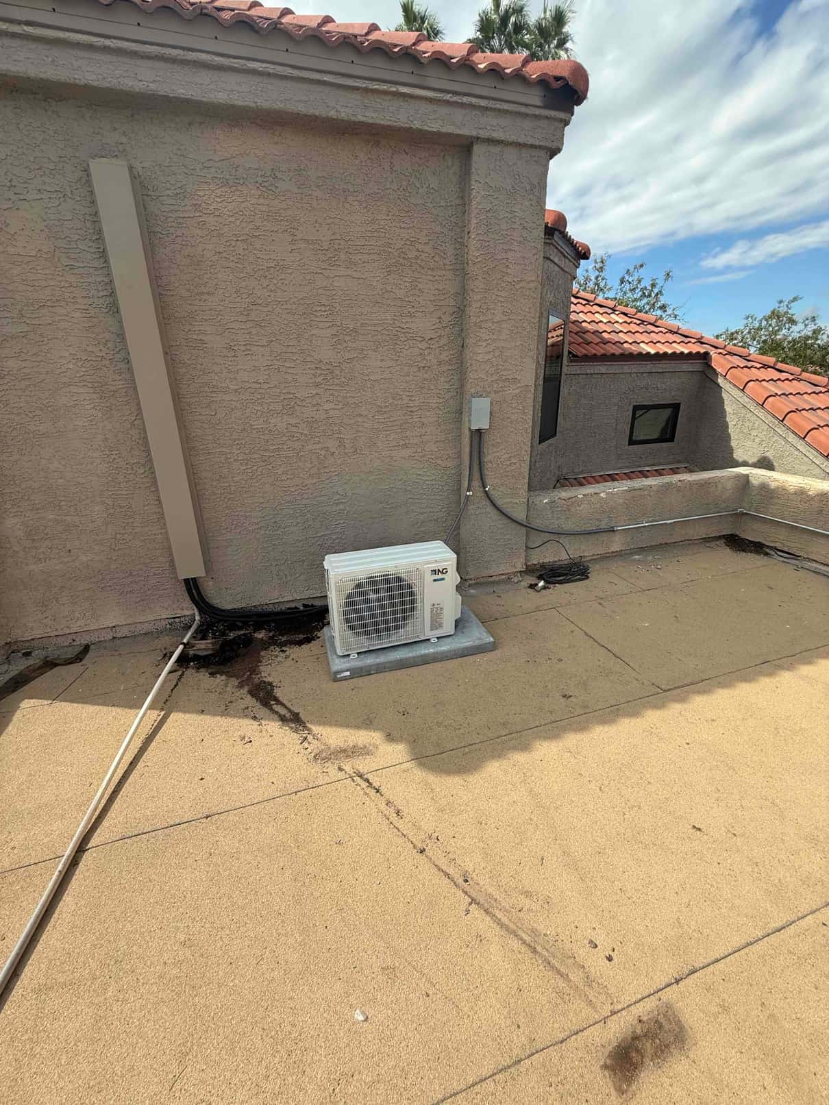 Mini-split outdoor condenser set on a rooftop pad with line set cover and electrical disconnect mounted on the wall.
