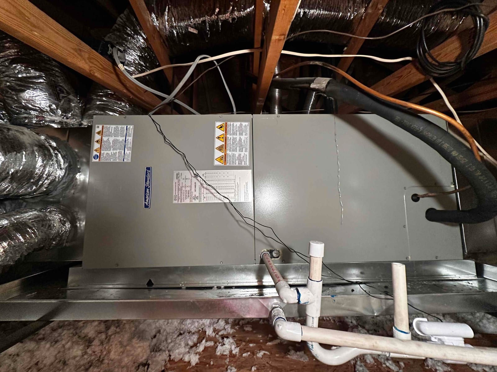 New air handler installed on a metal drain pan with insulated refrigerant lines, condensate piping, and flexible duct connections in the attic.