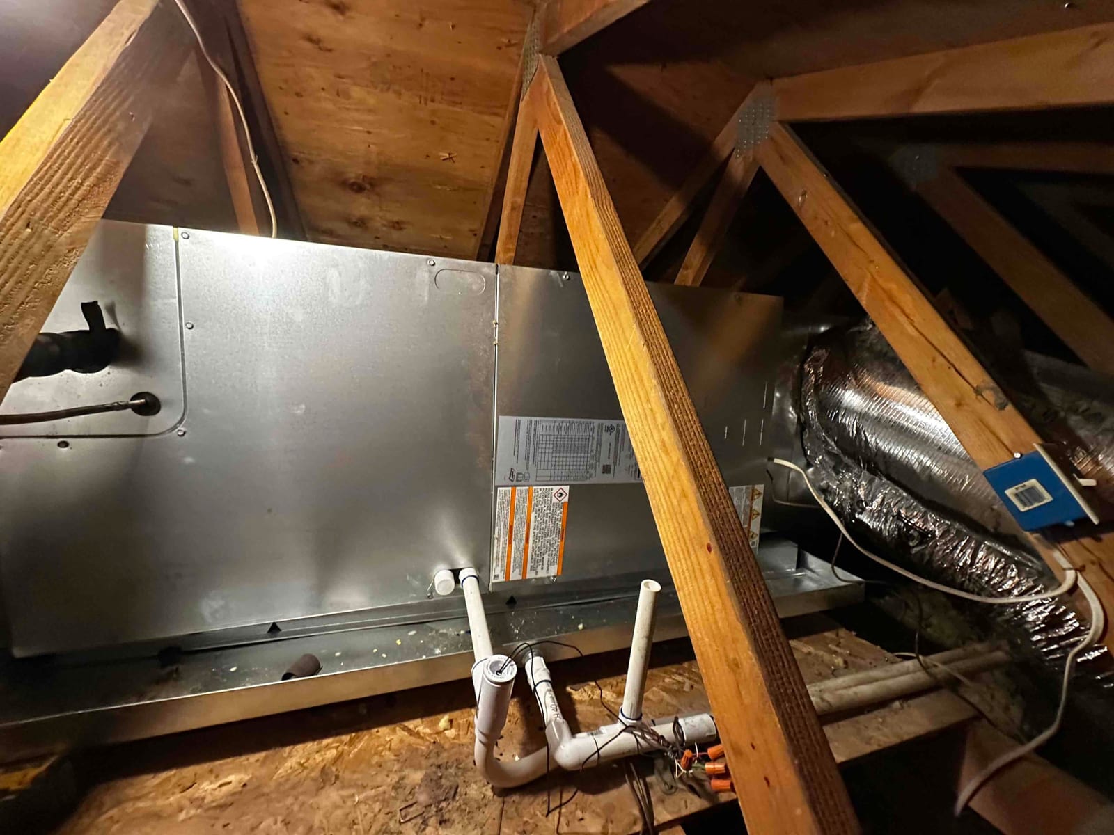 New air handler set in the attic with insulated supply duct, primary and secondary condensate drains, and electrical whip routed.