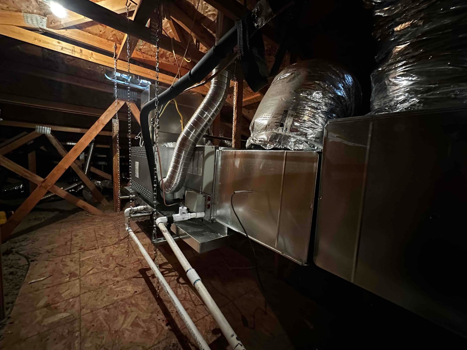 New horizontal air handler hung in attic with insulated ducts, condensate drain piping, and flexible connector installed and supported.