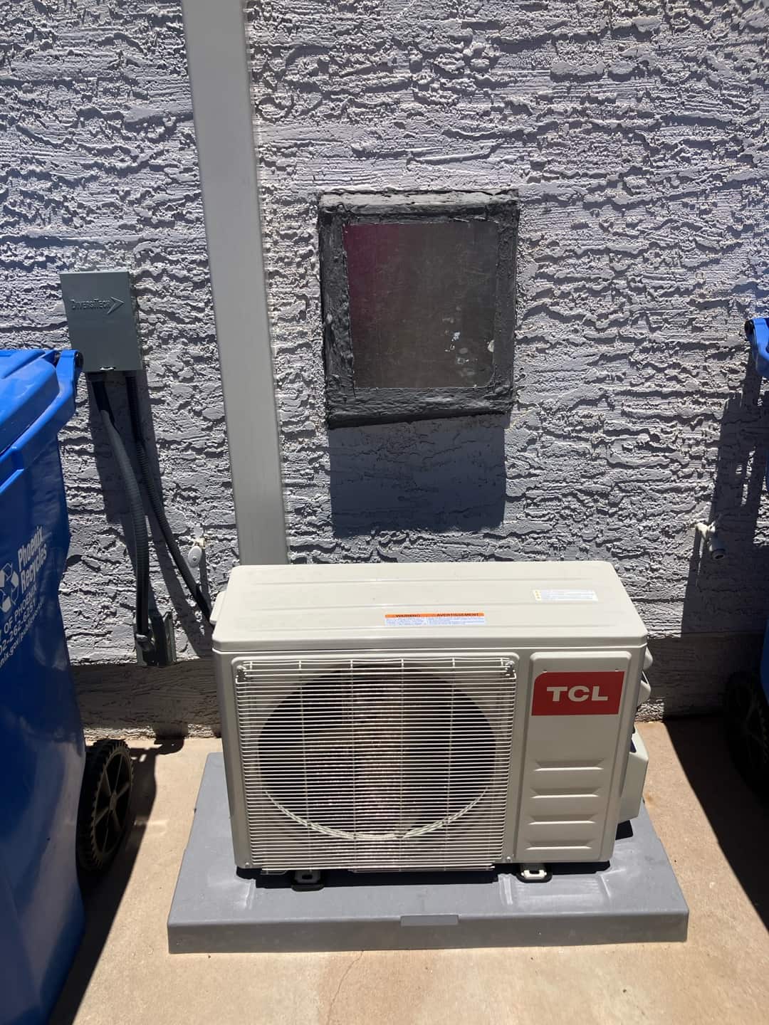 New mini-split condenser set on a level pad with weatherproof disconnect and line set cover installed against the exterior wall.
