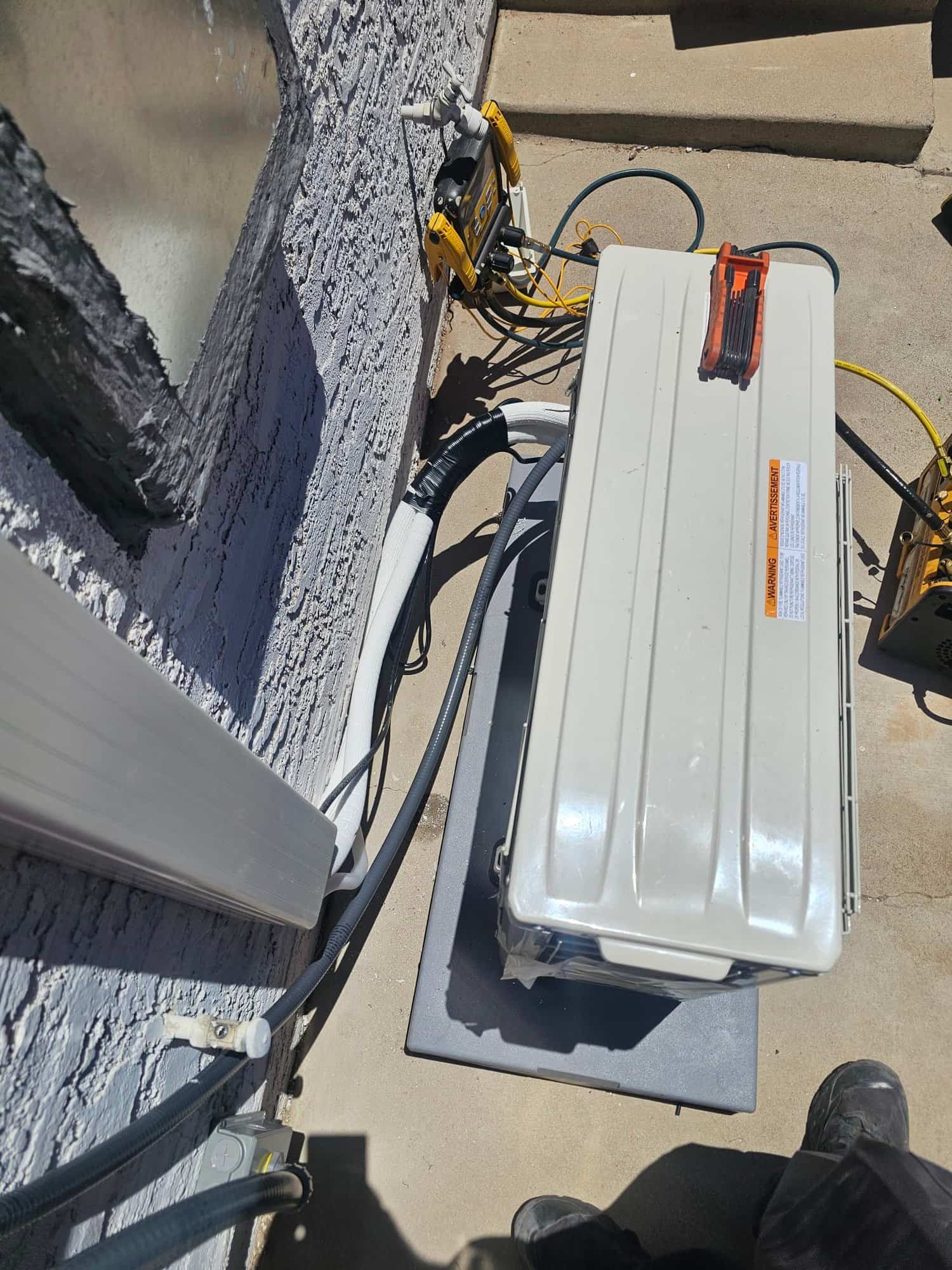 New mini-split outdoor unit set on a level pad with insulated line set and manifold gauges connected during commissioning.