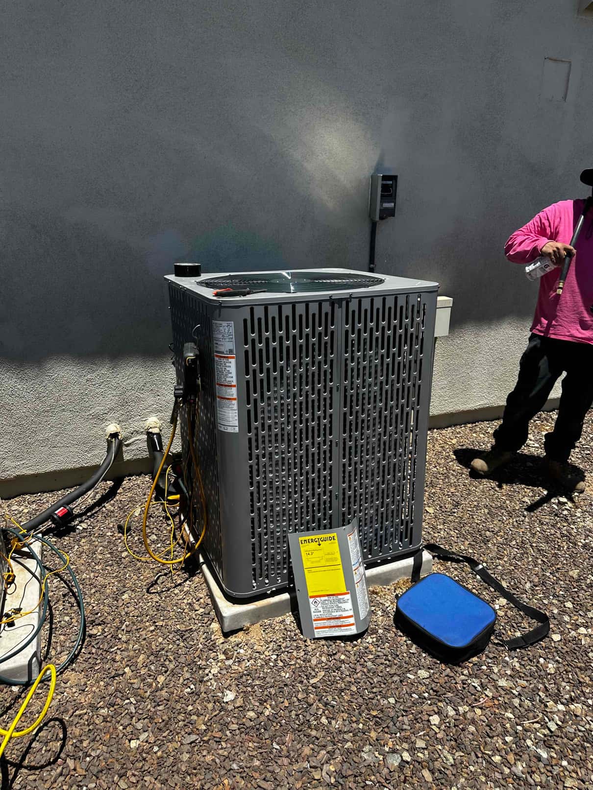 New outdoor condenser set on level pads with insulated line set and service ports accessible; installation materials staged nearby.