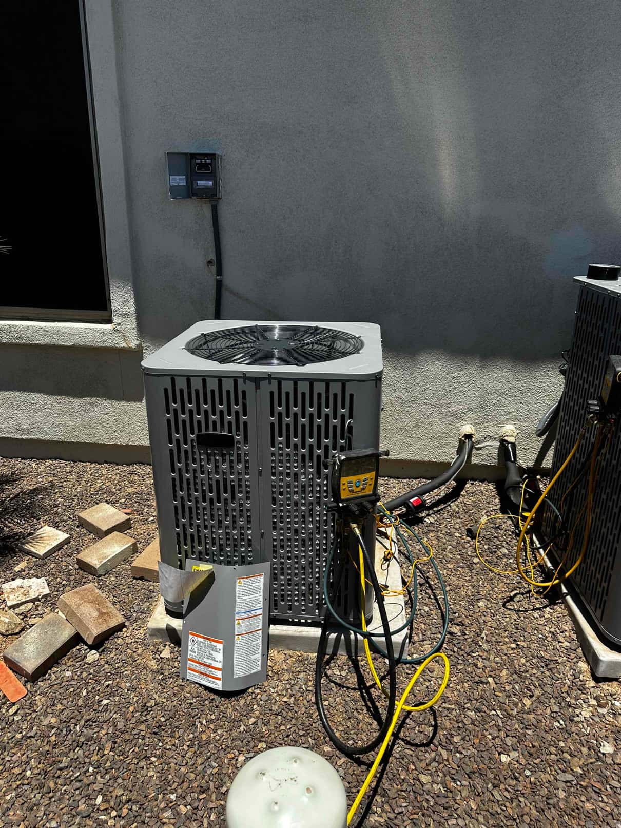 New outdoor condenser set on a pad with insulated line set, open disconnect, and digital manifold connected during commissioning.
