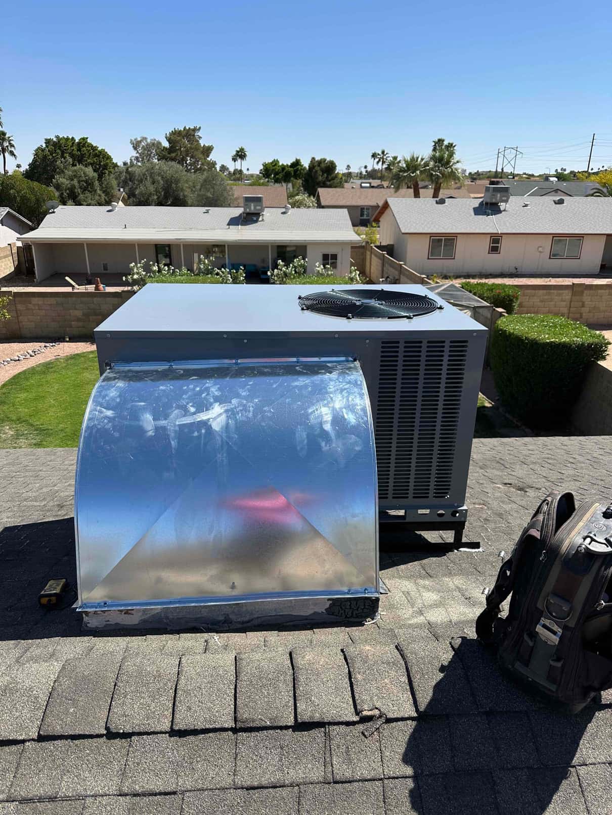 New 5-ton rooftop package unit set on shingles with a fabricated supply/return curb and sealed roof penetration visible.