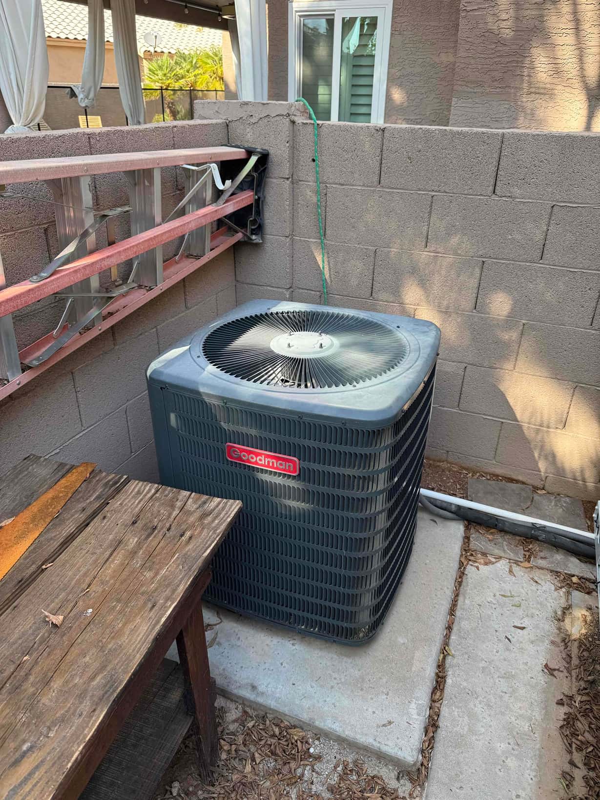 Outdoor air conditioning condenser on a concrete pad, with refrigerant and electrical conduits routed along the adjacent wall.