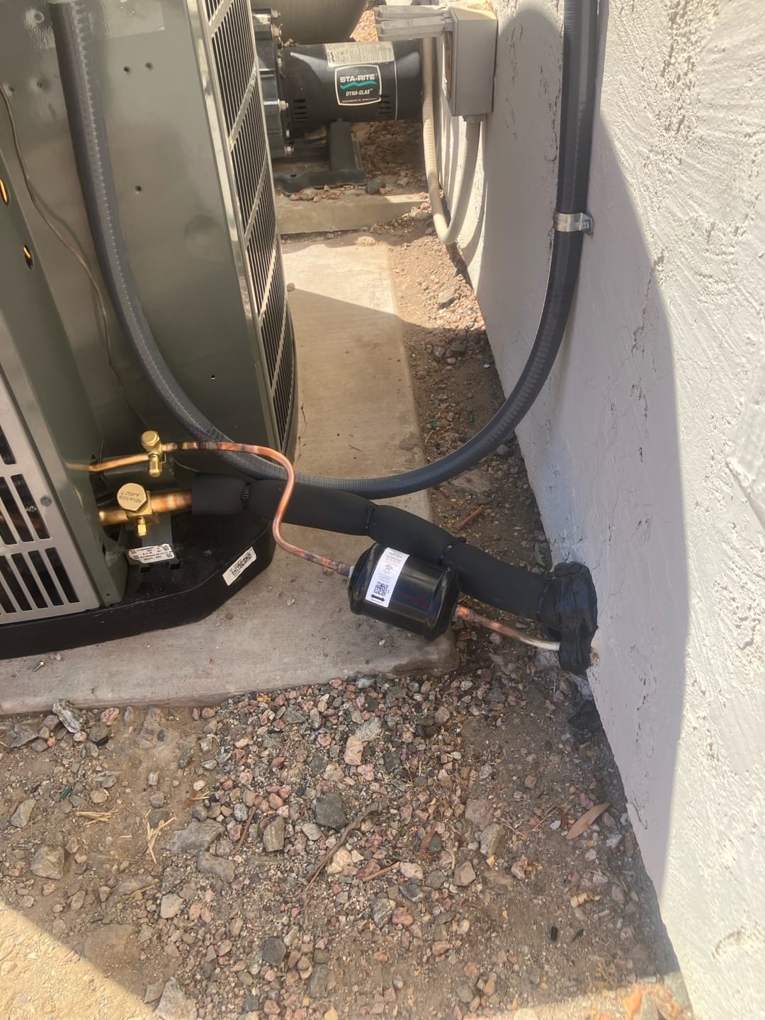 Outdoor heat pump set on a level pad with insulated refrigerant lines, suction accumulator, and sealed wall penetration.