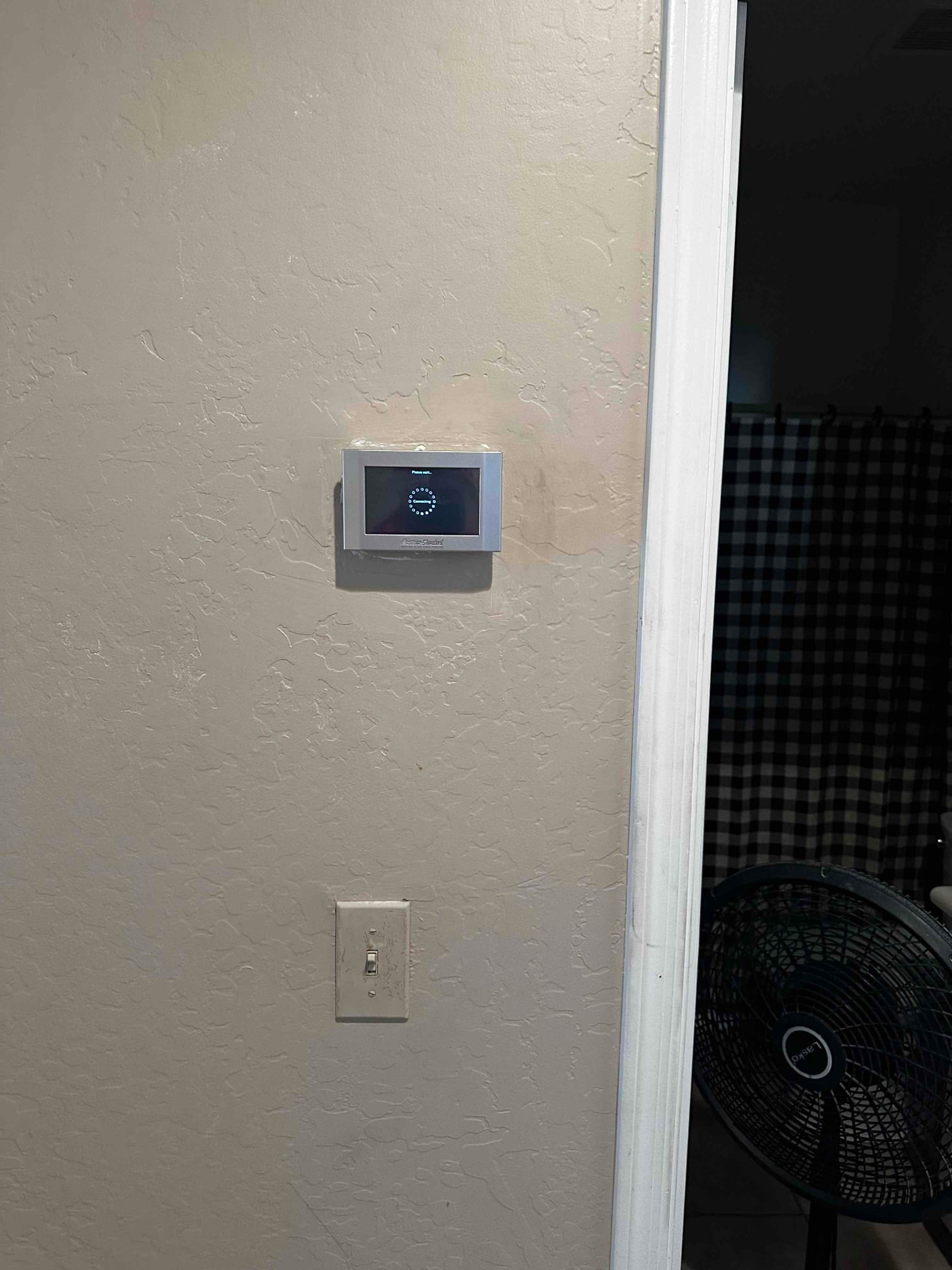 Wall-mounted digital thermostat installed and powered on inside the home, with adjacent light switch and doorway visible.
