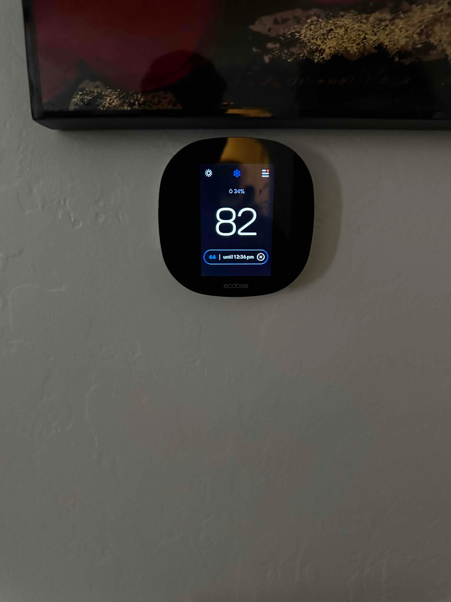 Wall-mounted smart thermostat installed and powered on, displaying indoor temperature of 82 degrees with cooling mode active.