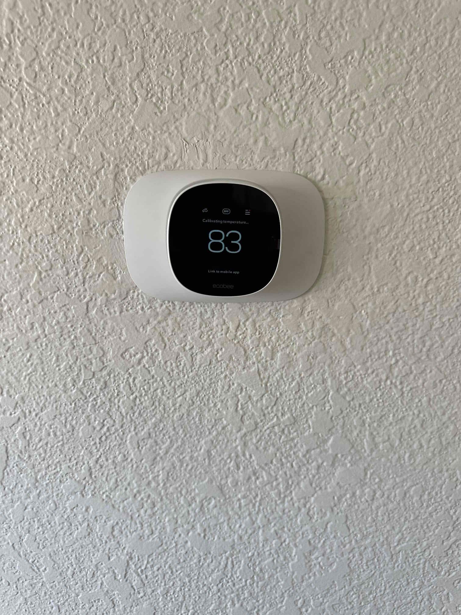 Wall-mounted smart thermostat installed and powering up, displaying a temperature calibration screen with 83 on the display.