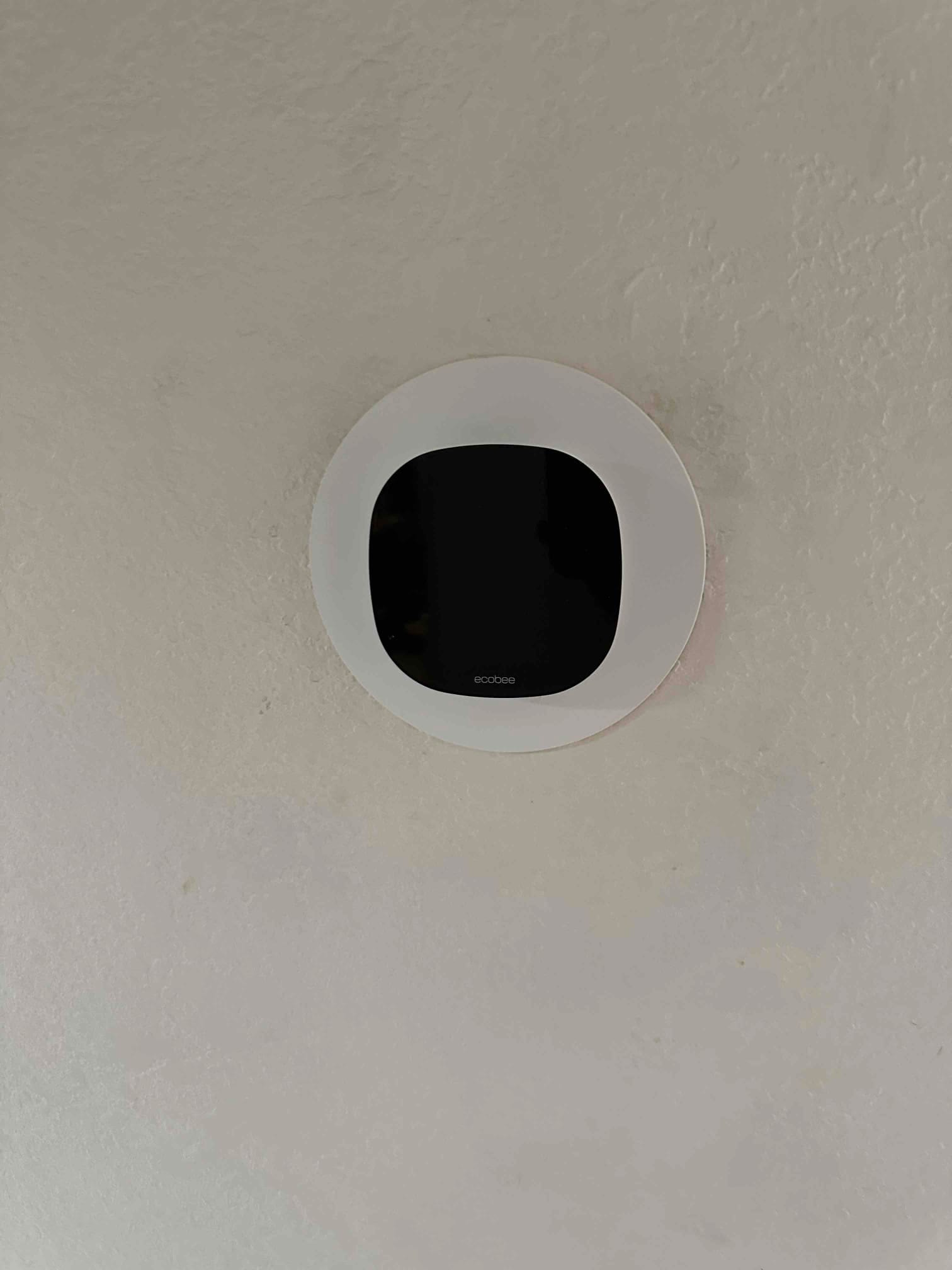 Wall-mounted smart thermostat installed with round trim plate, centered and flush on a finished interior wall.