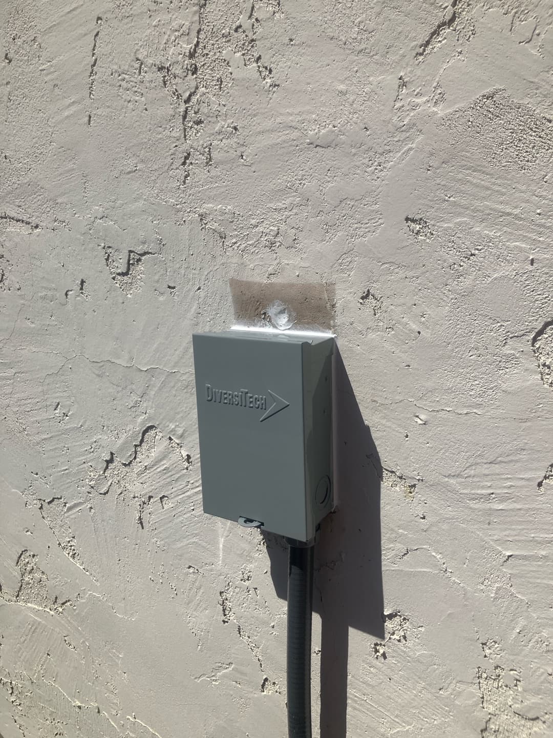 Weatherproof HVAC disconnect box mounted on exterior stucco wall with sealed conduit leading to the outdoor unit.