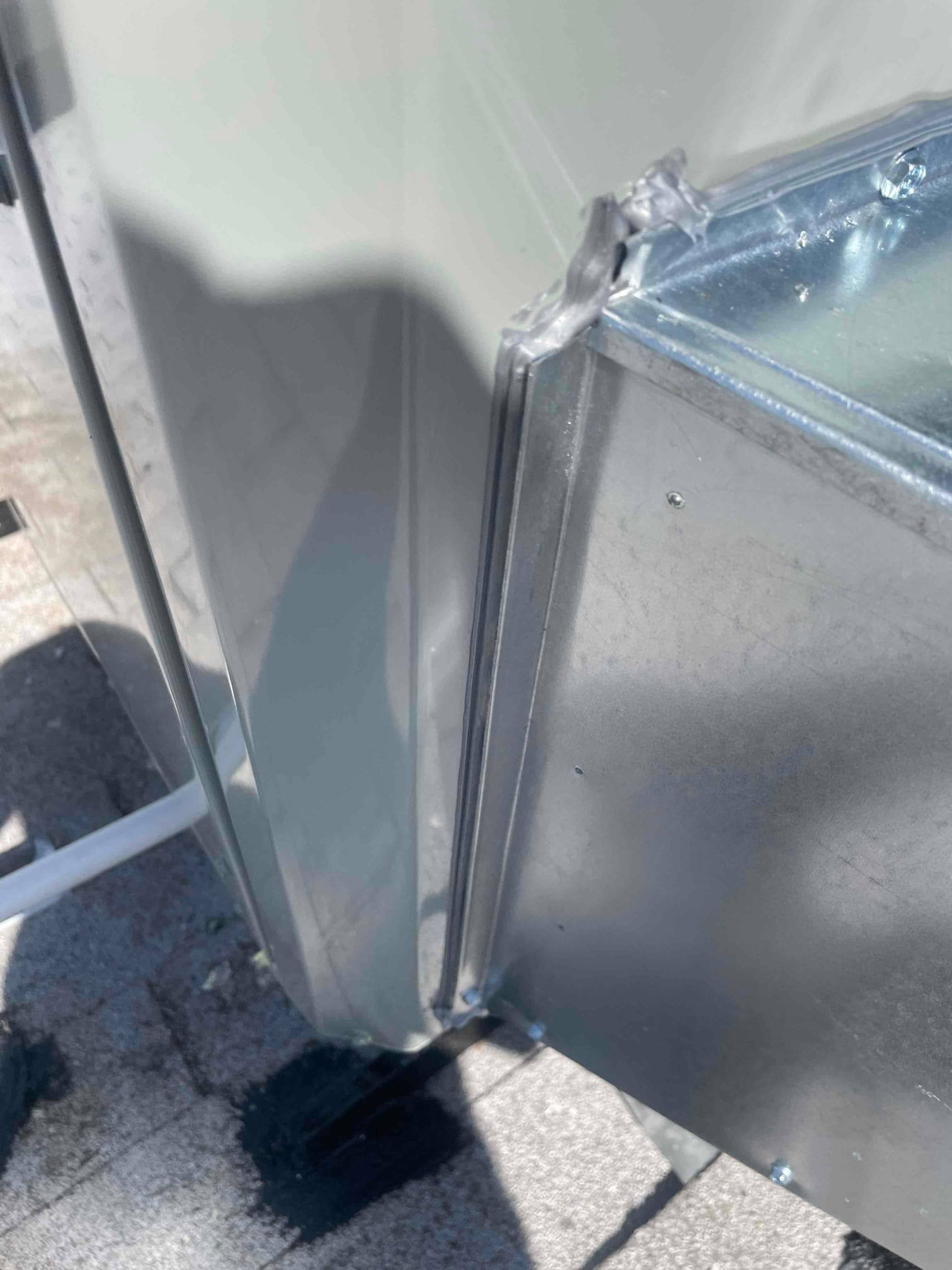Close-up of sealed sheet metal transition connecting new condenser cabinet to a galvanized duct plenum on the rooftop.