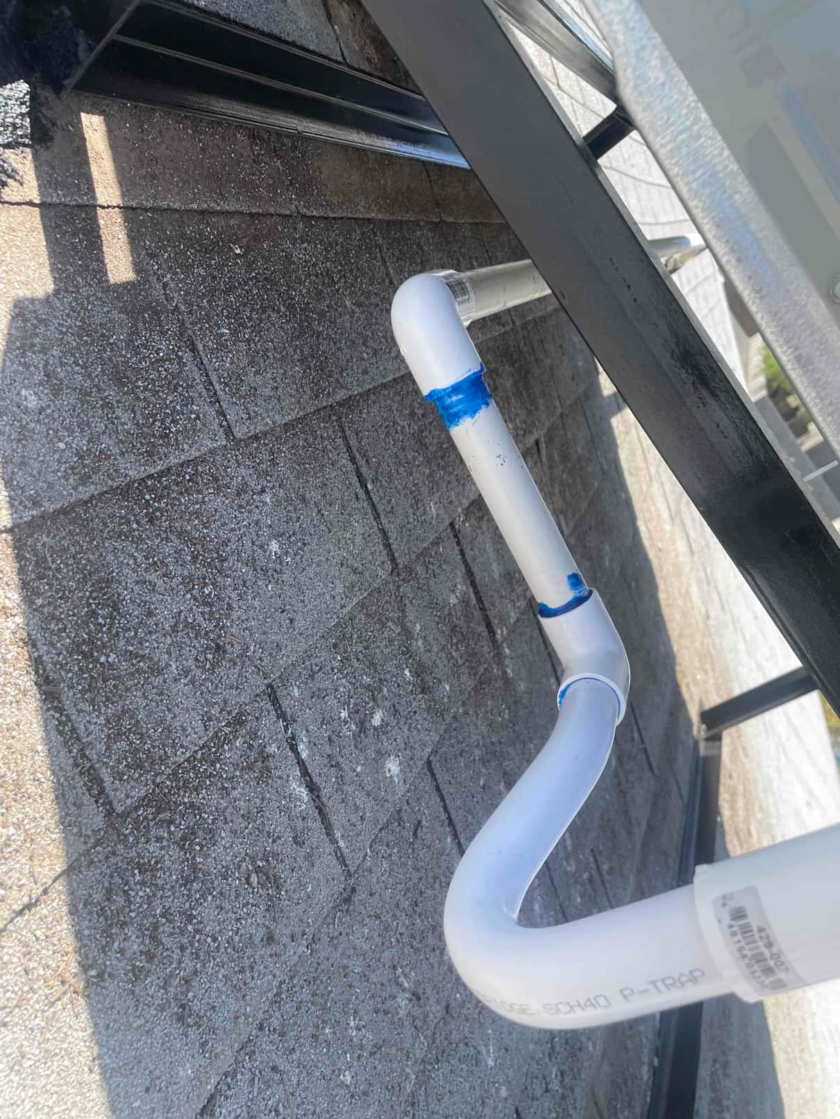 Condensate drain assembly with PVC P-trap and glued fittings installed beneath rooftop HVAC unit support rails.
