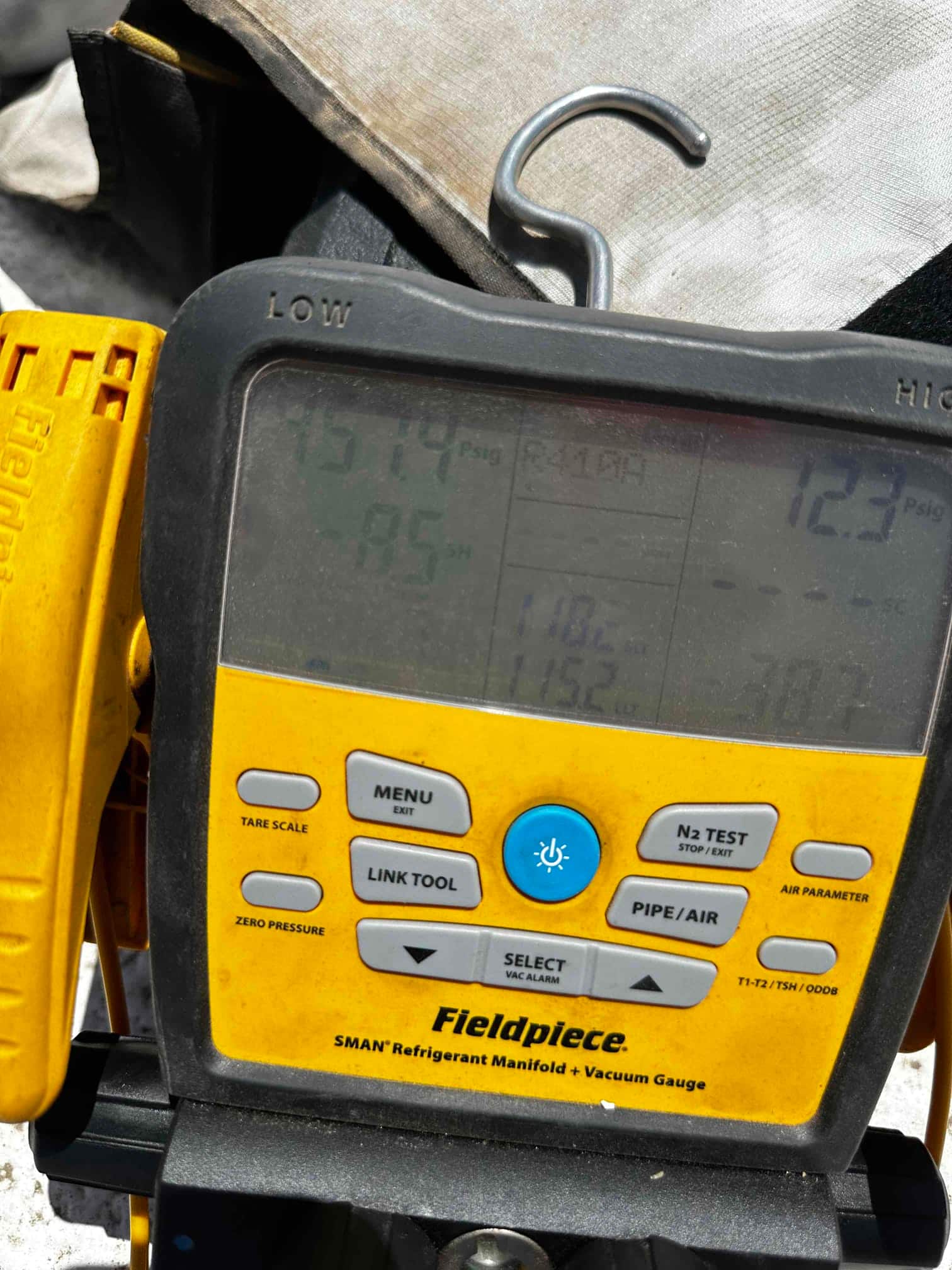 Digital refrigerant manifold meter close-up during setup, screen glare obscuring pressure readings and test status.