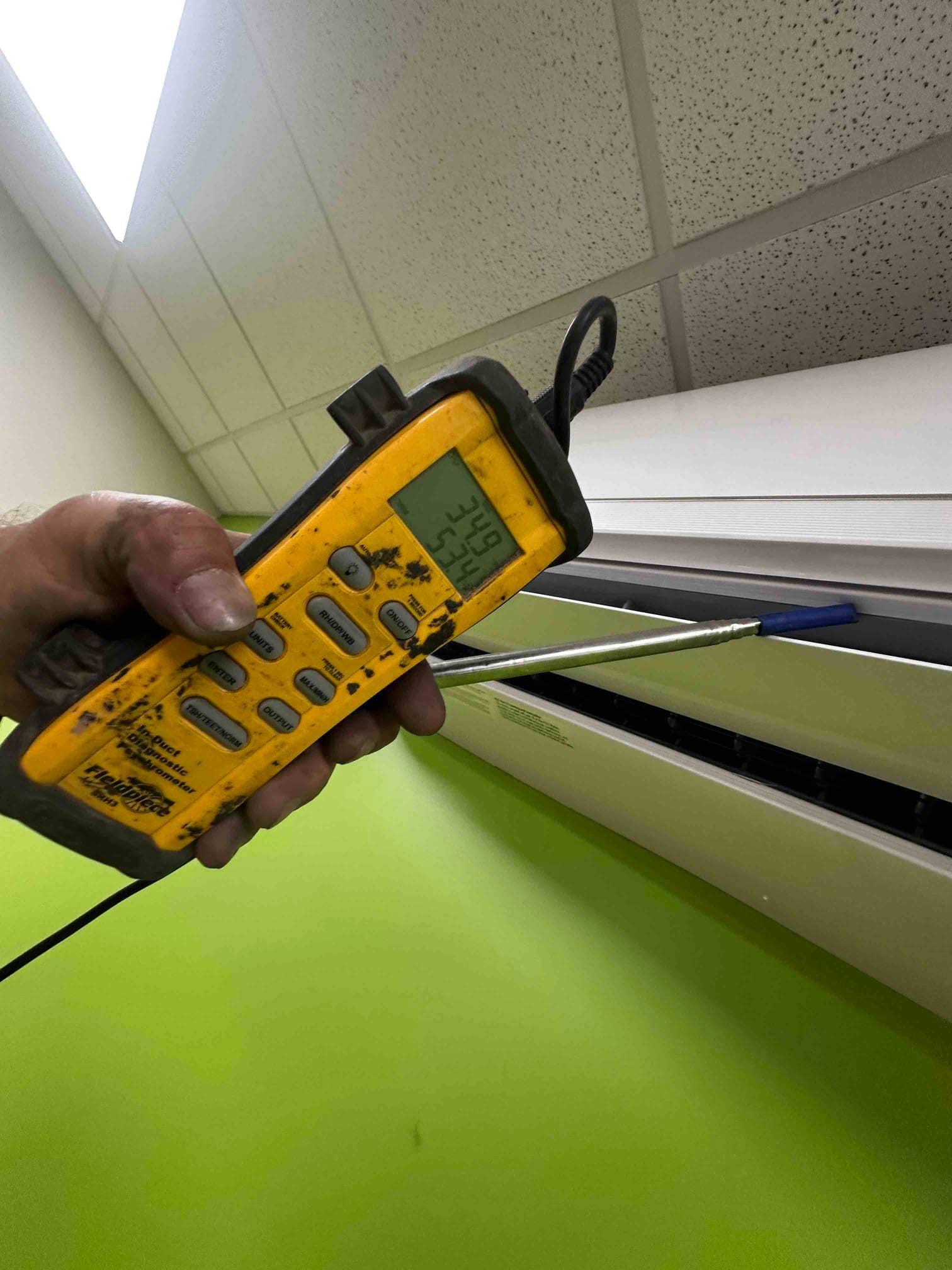 Digital thermometer probe measures supply air temperature at the mini-split indoor unit discharge during commissioning.