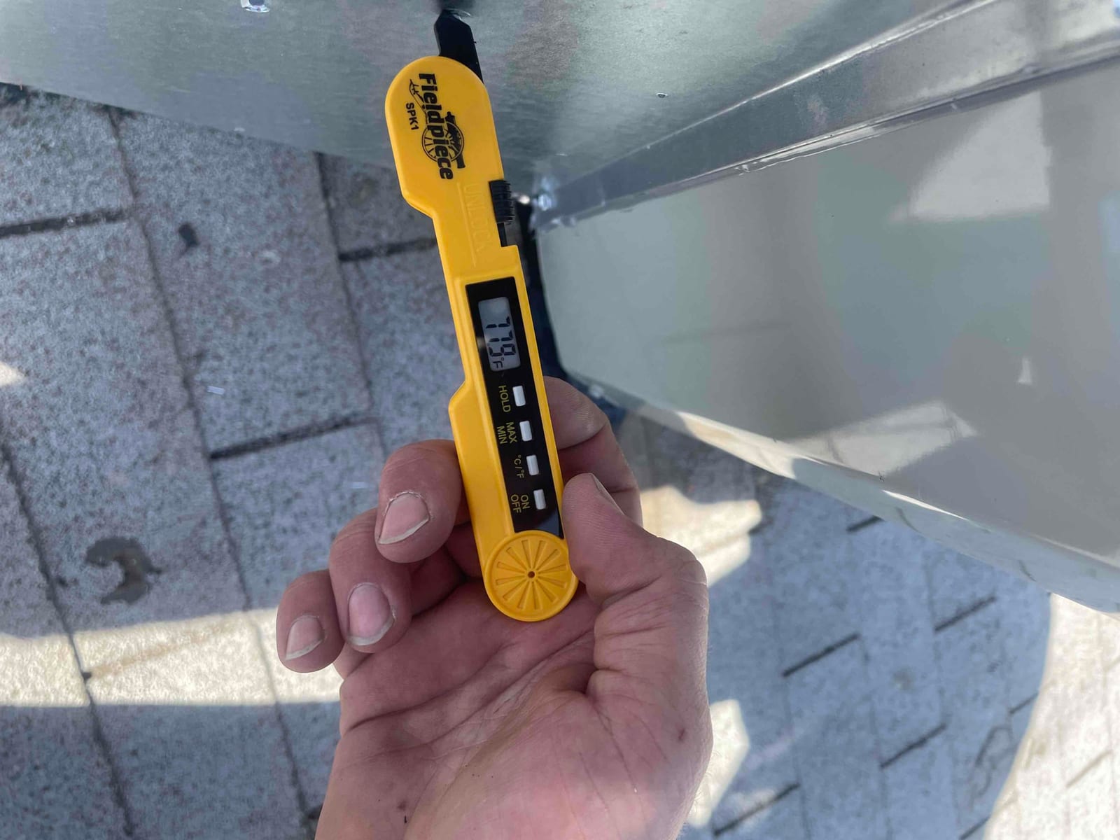 Digital thermometer probe shows 77.9°F while measuring air temperature at the duct during commissioning.