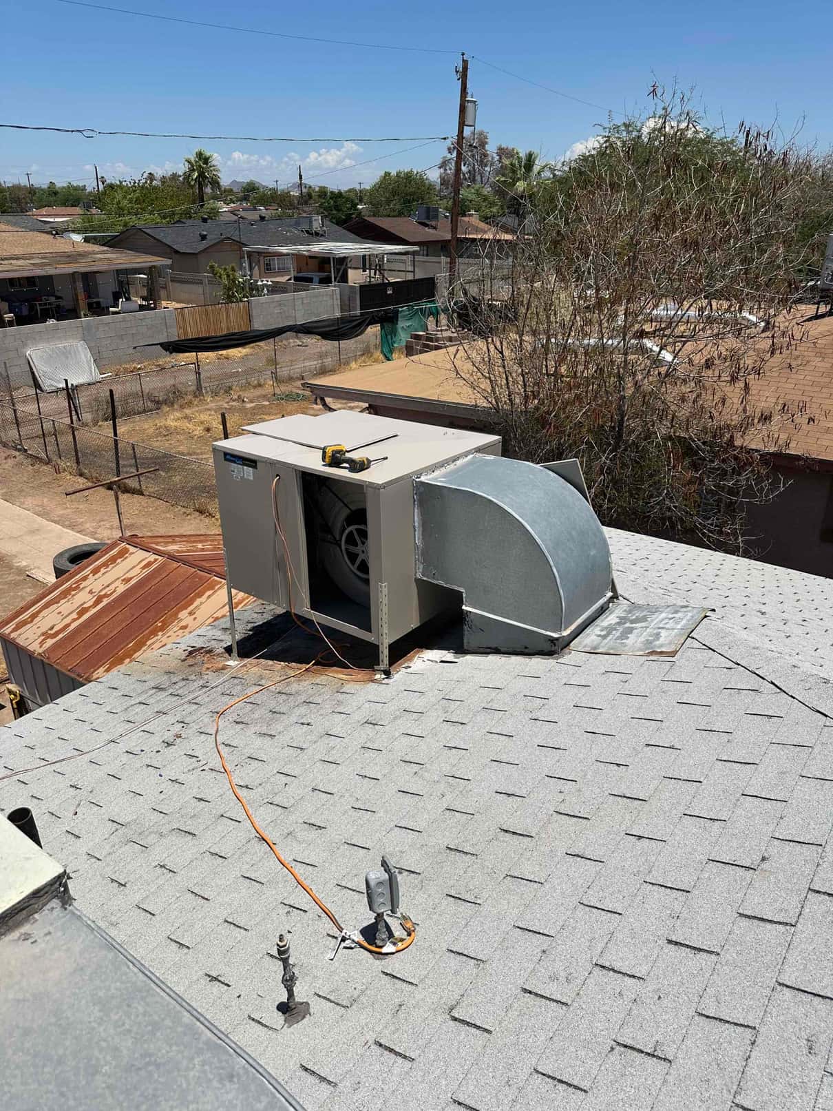 Evaporative cooler installed on rooftop with duct transition and electrical whip routed, showing completed curb and roof penetration.