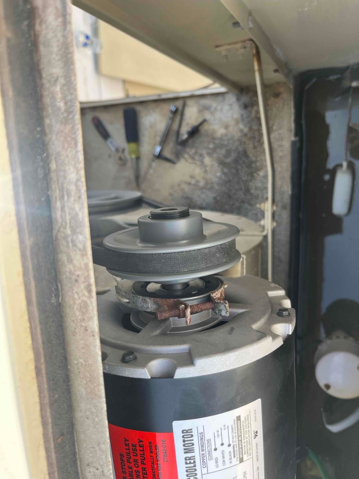 Evaporative cooler motor installed with pulley and belt, showing exposed winding area and mounted within the unit housing.